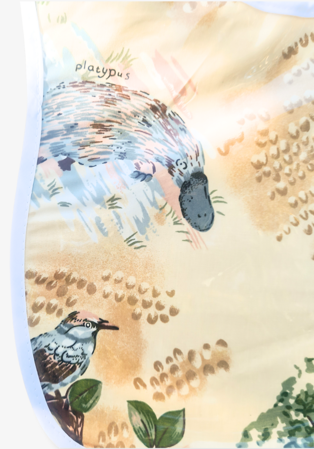Laminated baby feeding bib featuring illustrated native Australian animals, including a platypus and birds, with a soft white trim and snap closure, laid flat on a grey background.