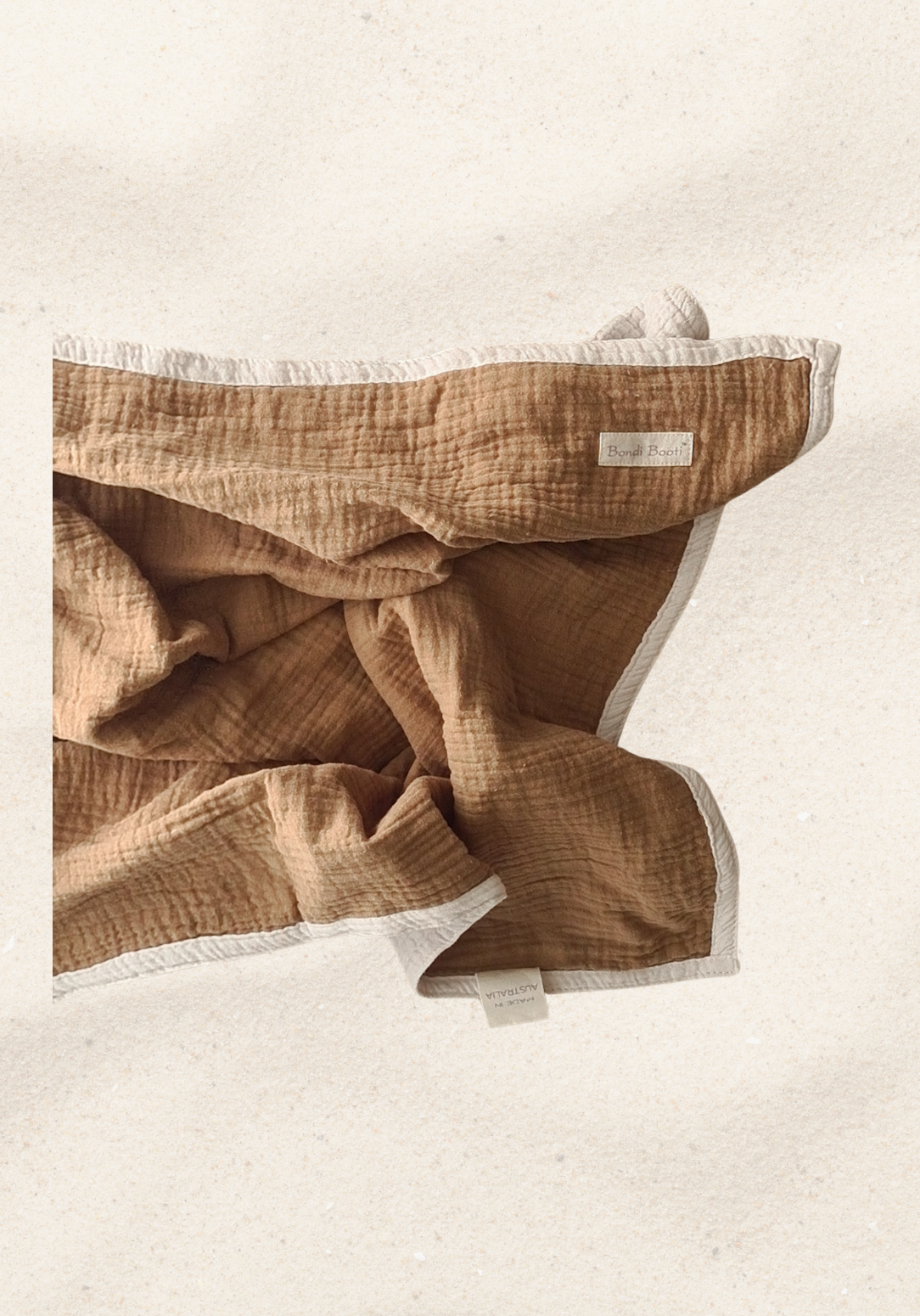 Reversible baby blanket in warm brown and white organic cotton, with visible Bondi Booti and “Made in Australia” labels, displayed on a neutral fabric background.