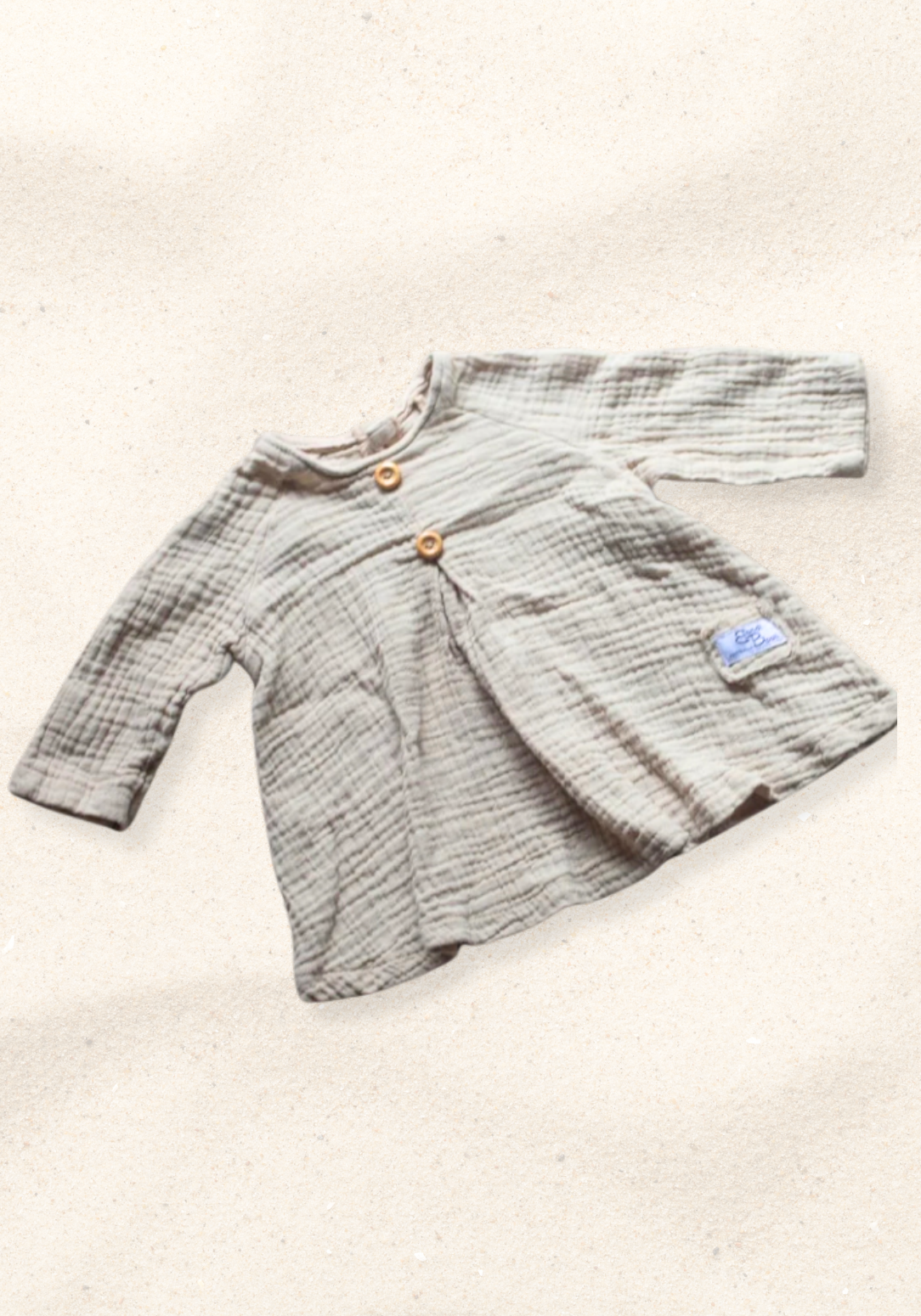 Boho-style baby dress in beige with embroidered hem, made from breathable cotton and displayed on a sand background