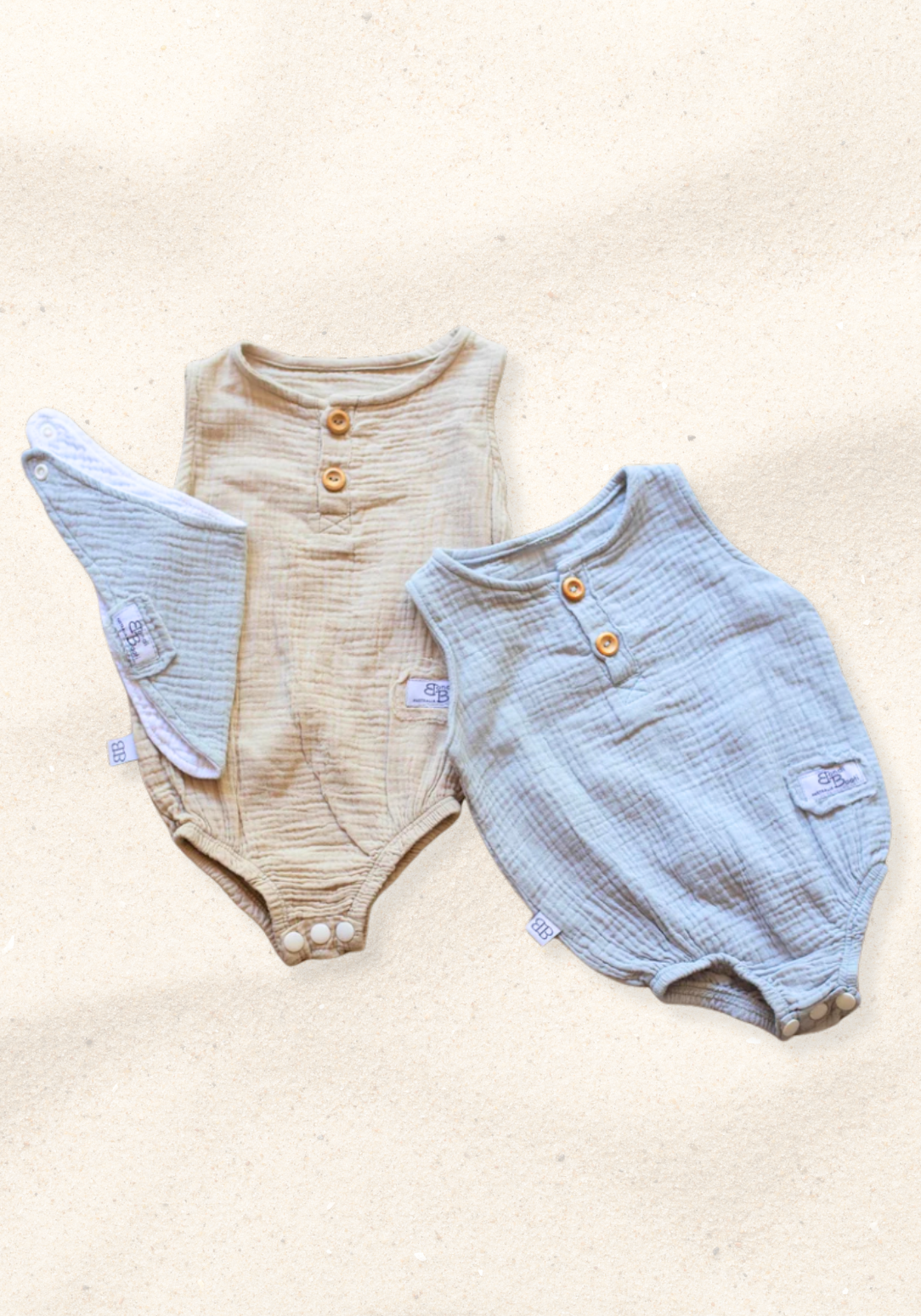 Beige baby romper made of organic cotton with wooden button front and soft texture, displayed on a sand background
