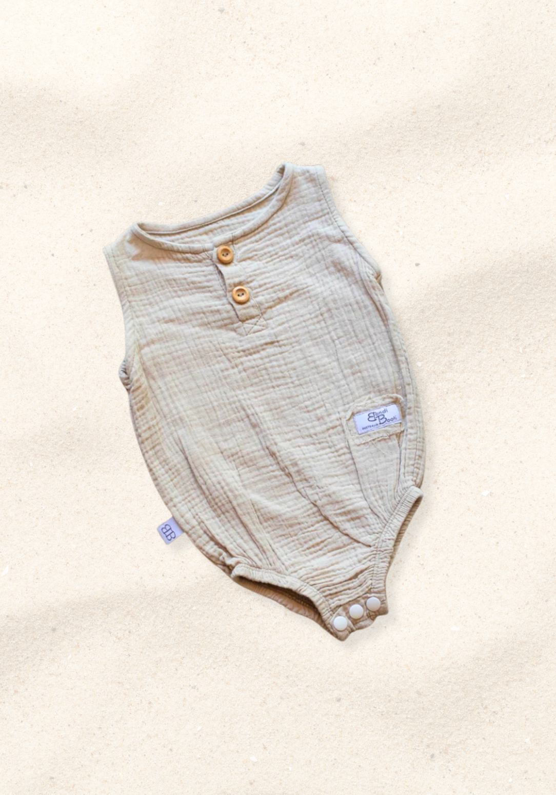 Beige baby romper made of organic cotton with wooden button front and soft texture, displayed on a sand background