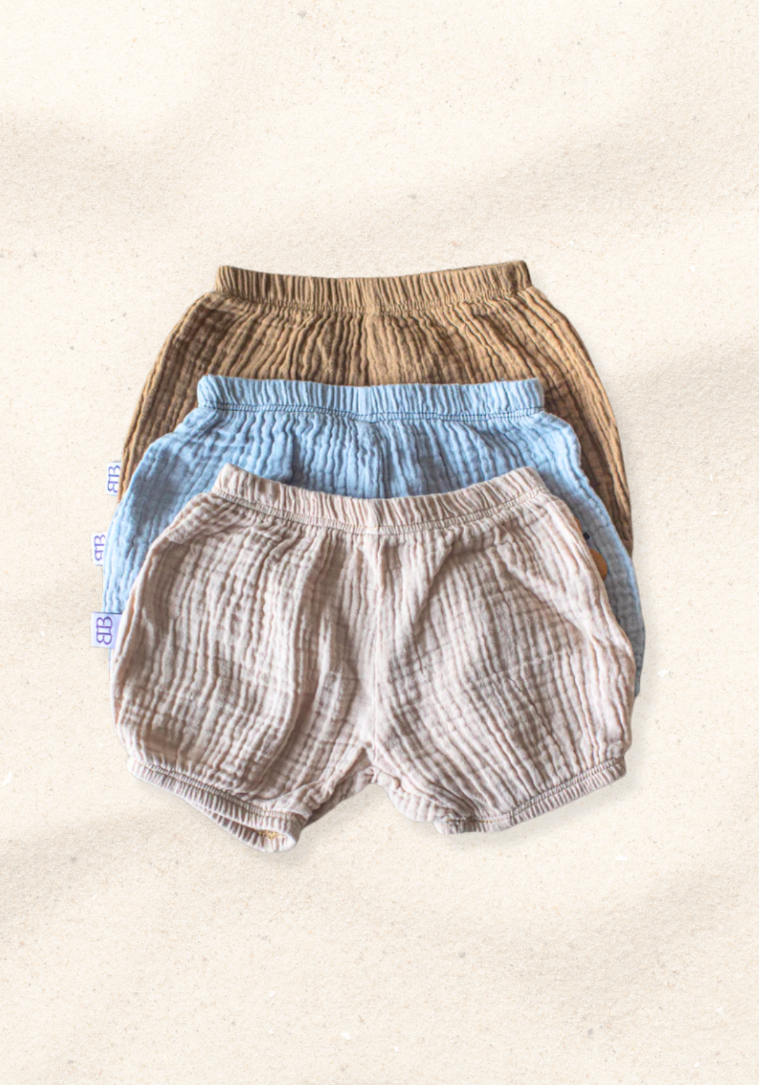 Three-pack of organic cotton baby bloomers in assorted neutral tones with elastic waist and leg openings