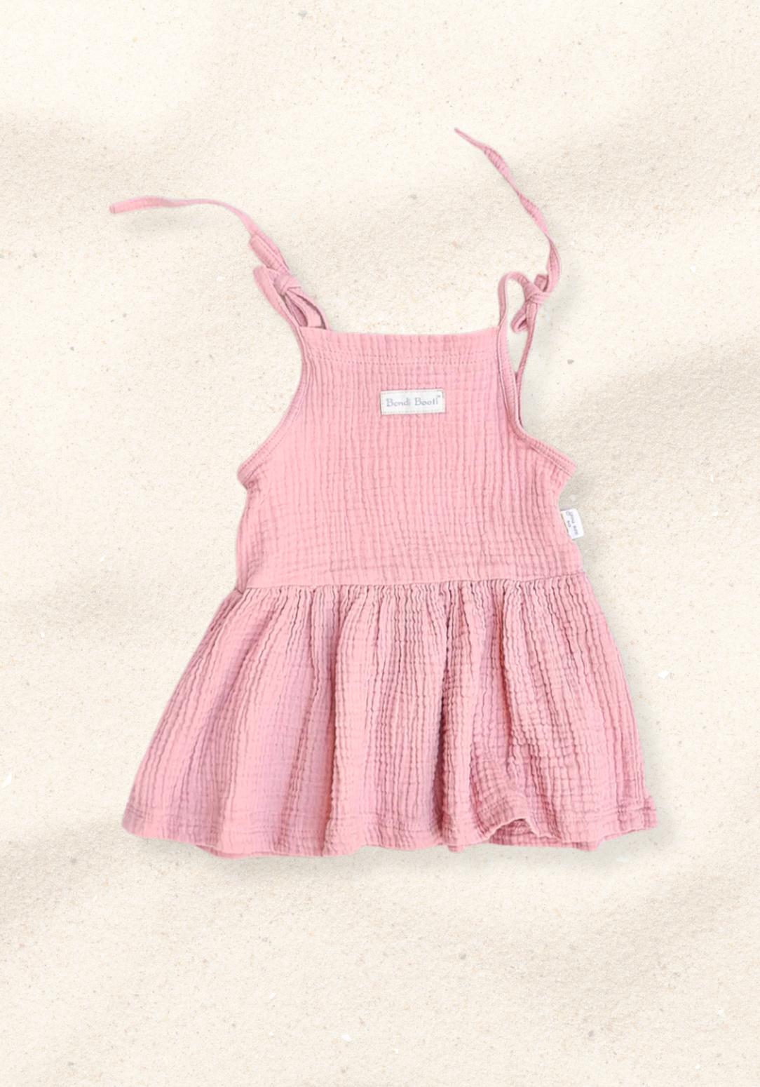 Dusty pink baby picnic dress with ruffled sleeves and gathered waist, made from soft cotton and laid flat on a sand-colored background