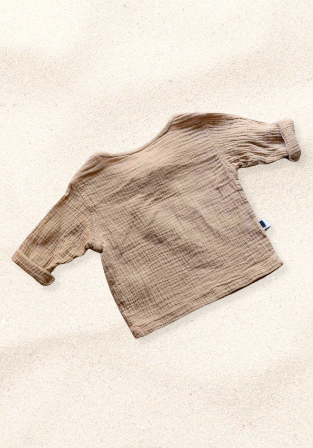 Mocha-colored pirate-style baby shirt with wooden buttons and long sleeves, laid flat on a sand-colored background